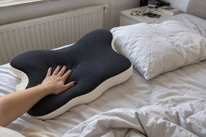 Hand drückt in ein Nackenkissen aus Memory Foam neben einem normalen Kopfkissen